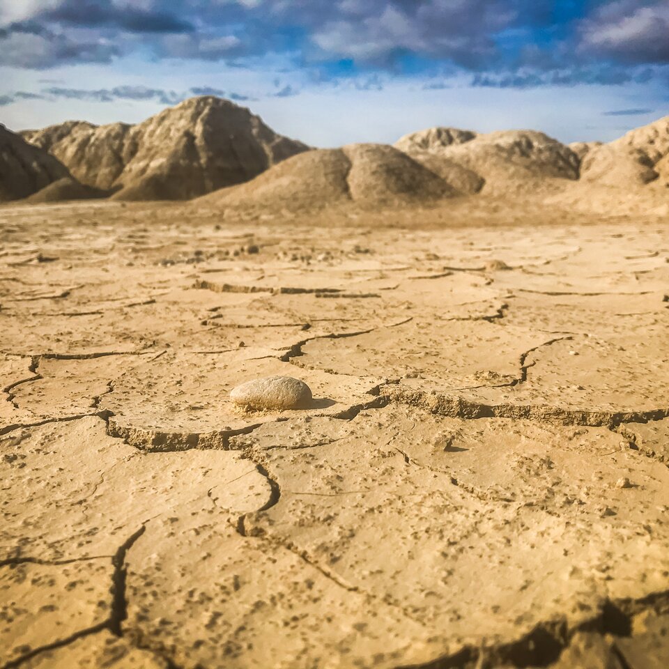 Bild från reseberättelse om en resa till Pyrenéerna med husbil visar sandig, torr mark med sprickor, i bakgrunden syns kullar.