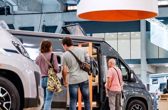 Besucher vor Carado Wohnmobil auf Messe, mit geöffnetem Campervan und Carado Logo über dem Stand