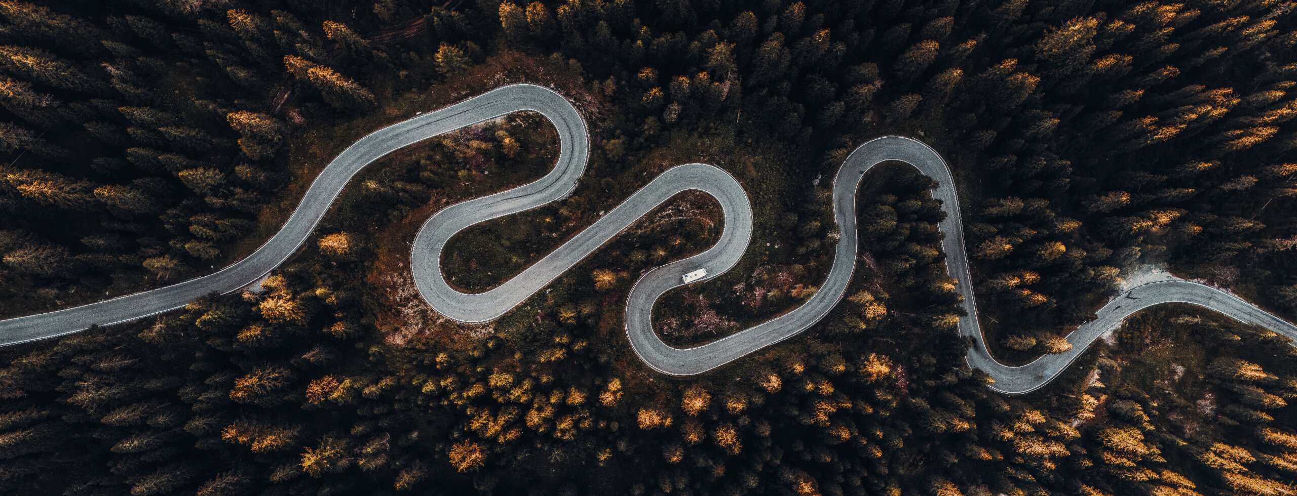 Aerial view of a winding mountain road with a motorhome in a dense forest