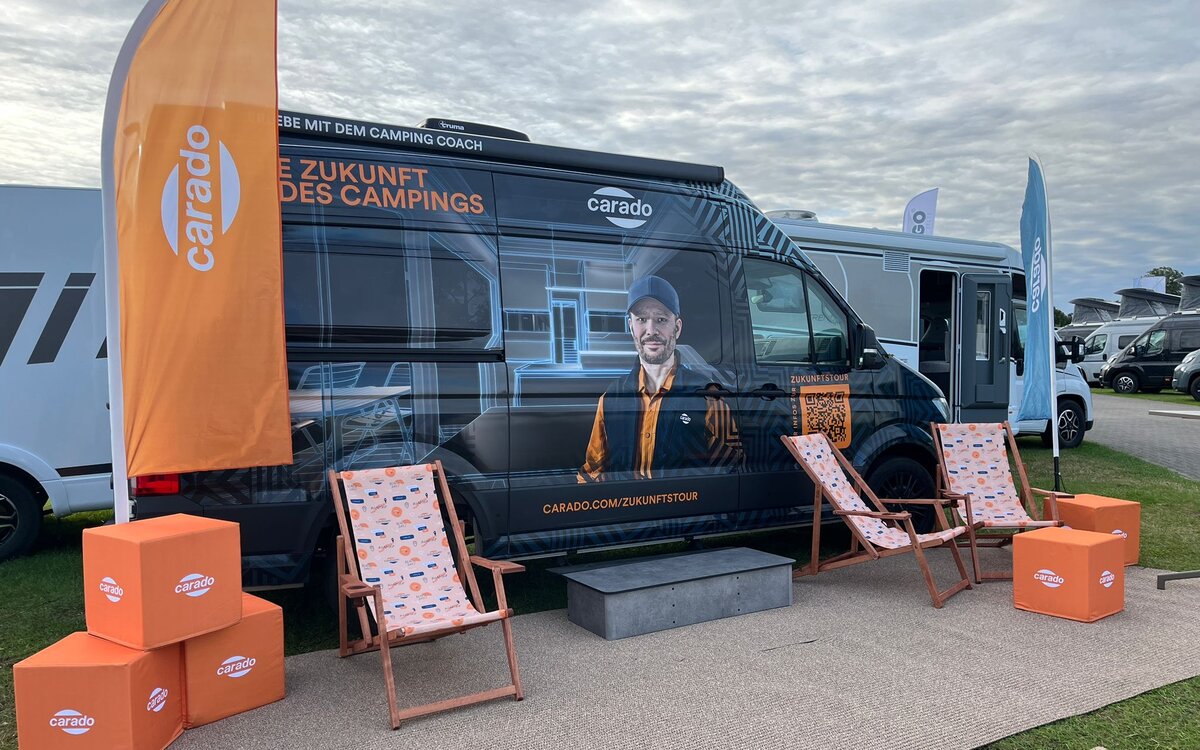 Carado Campervan auf Messegelände mit Werbegrafik, Fahnen und Liegestühlen vor dem Fahrzeug