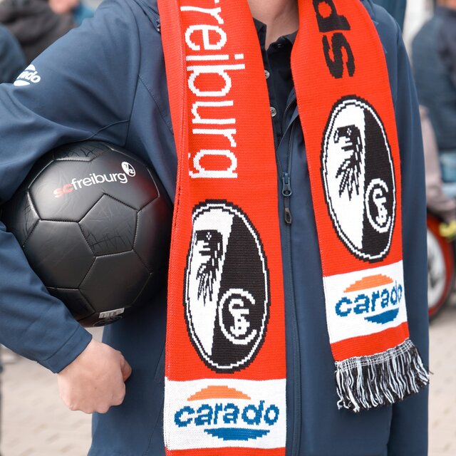 Person with an SC Freiburg scarf and black football at a Carado event