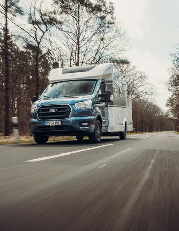 Carado motorhome, front view, driving along a country road through the forest