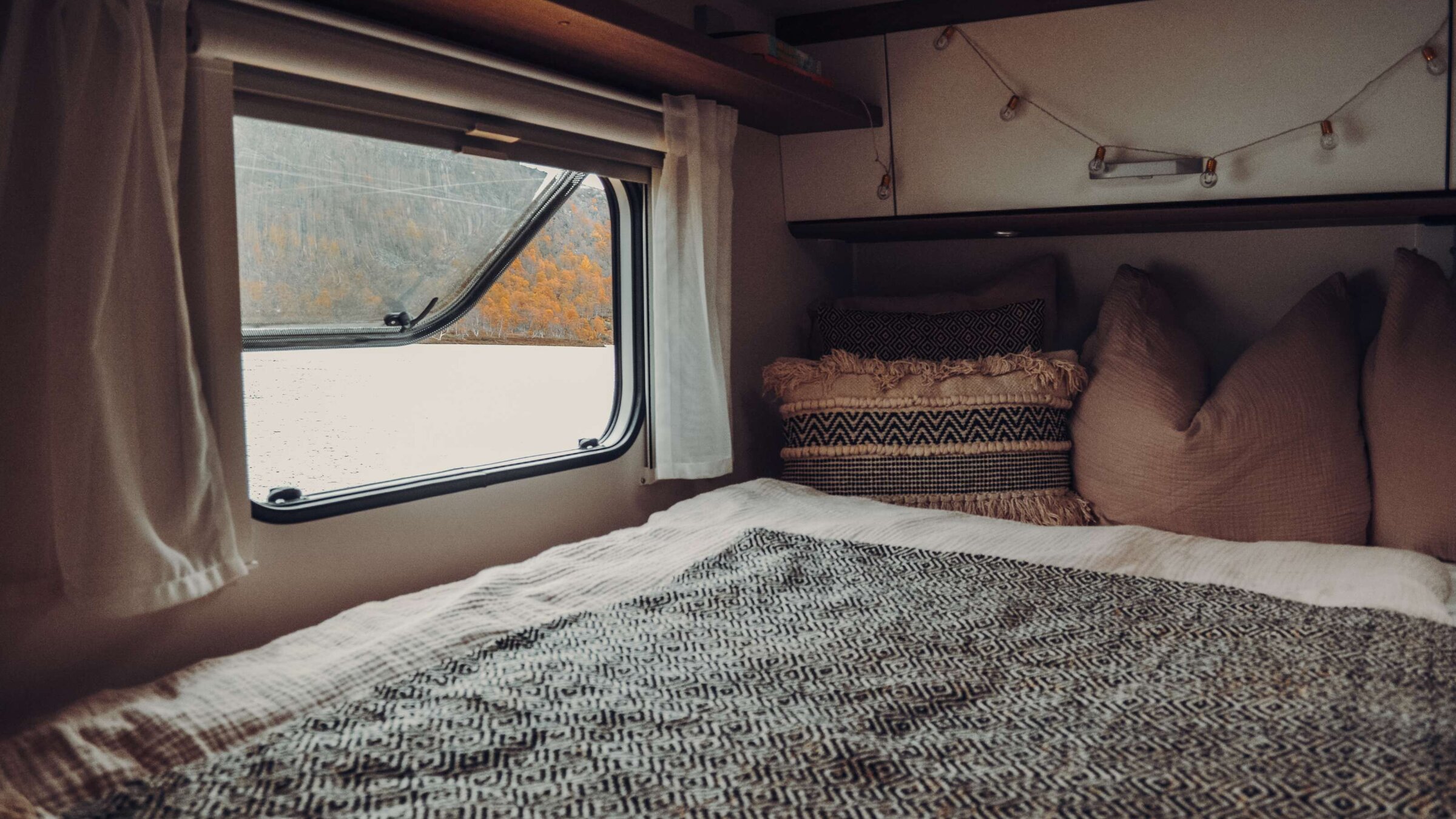 Sleeping area in the Carado motorhome with bed, pillows, overhead cabinet and side window