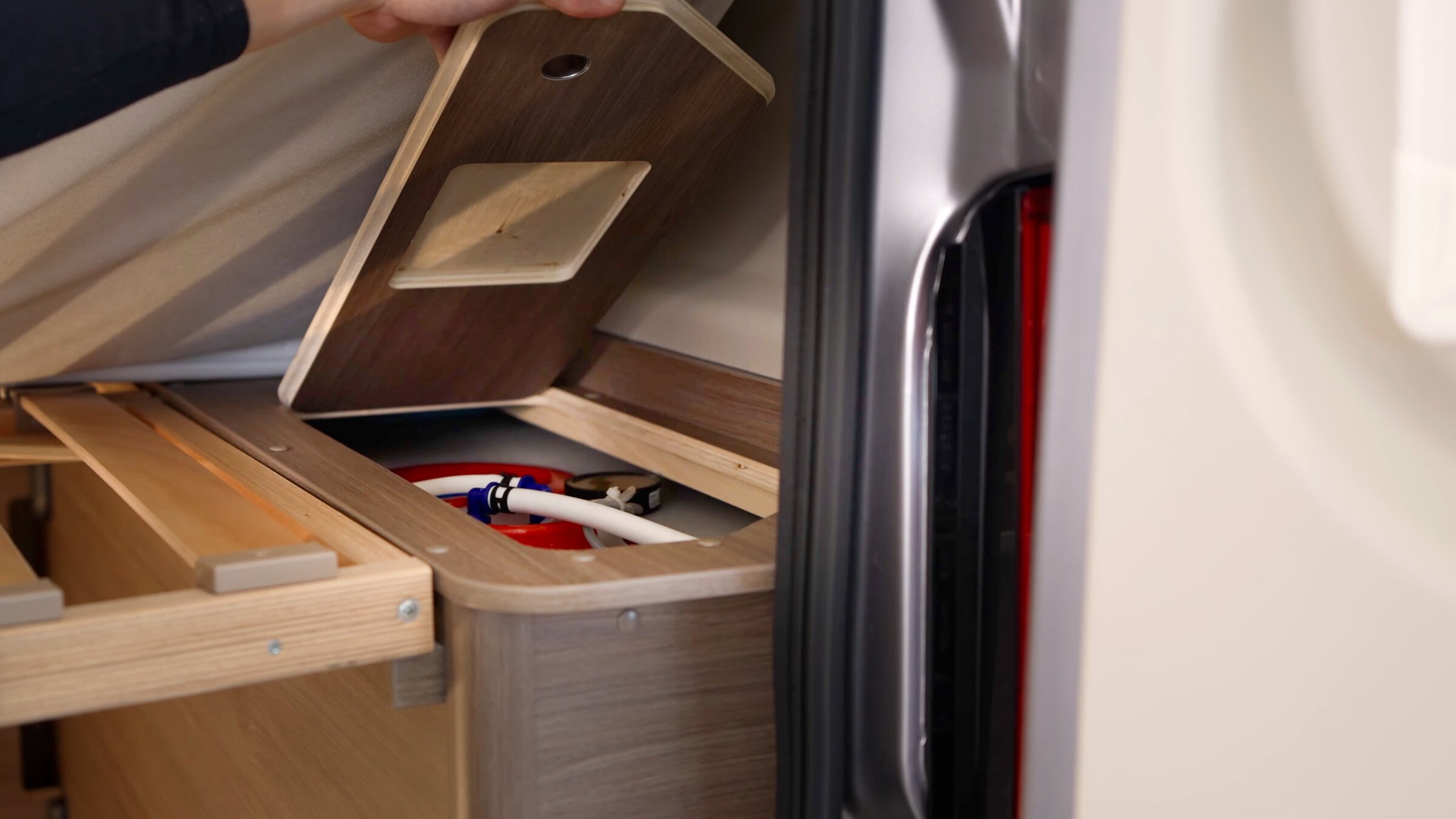 Compartiment de rangement dans un camping-car Carado sous un couvercle relevé, avec raccords visibles et cadre en bois