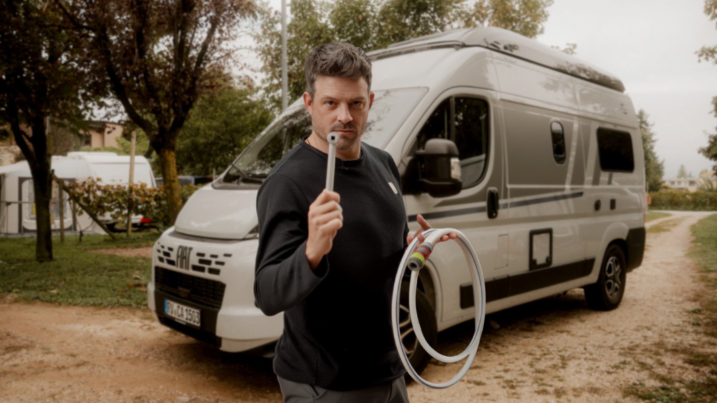 Personne avec tuyau et raccord devant un camping-car Carado sur le camping