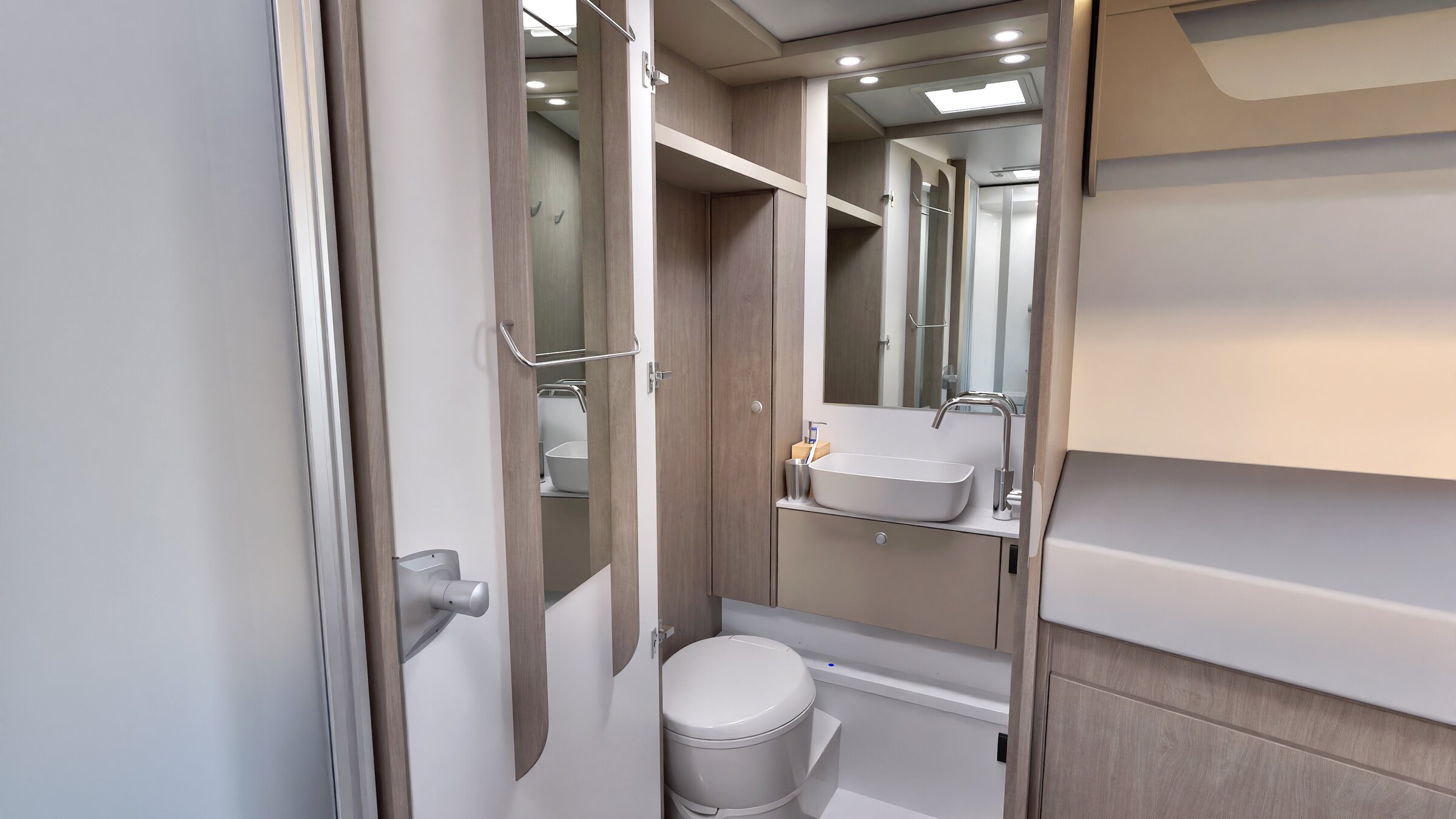 Carado motorhome bathroom with washbasin, mirror, toilet and wooden cabinets next to single bed