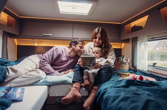 Une famille avec un jeune enfant lit dans le lit arrière d'un camping-car Carado