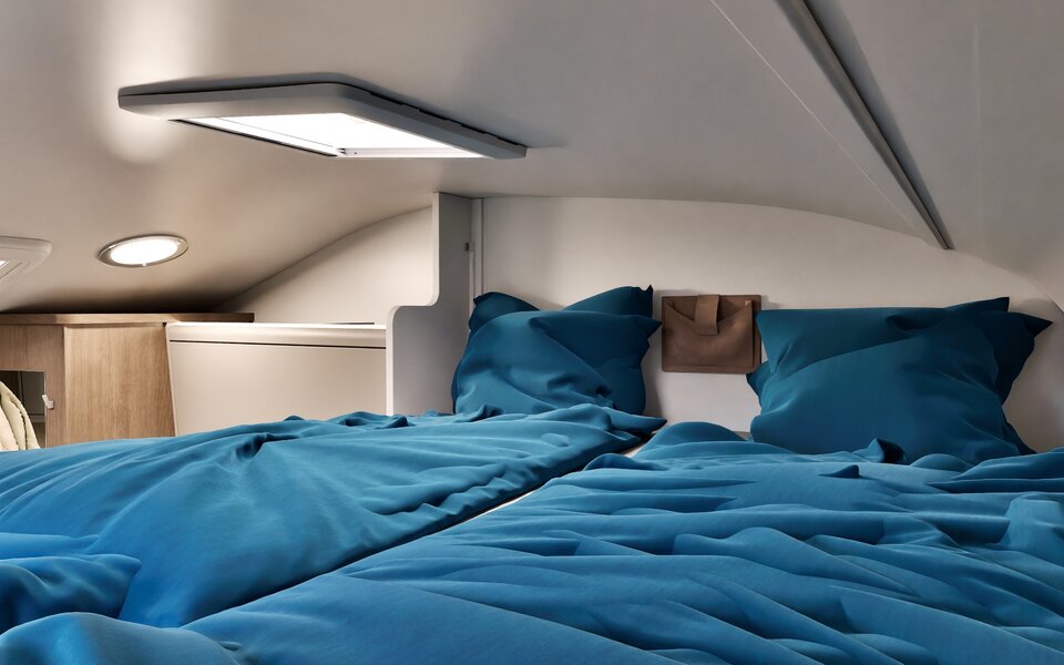 Sleeping area in a Carado motorhome with a double bed, blue bedding, roof window and LED lighting