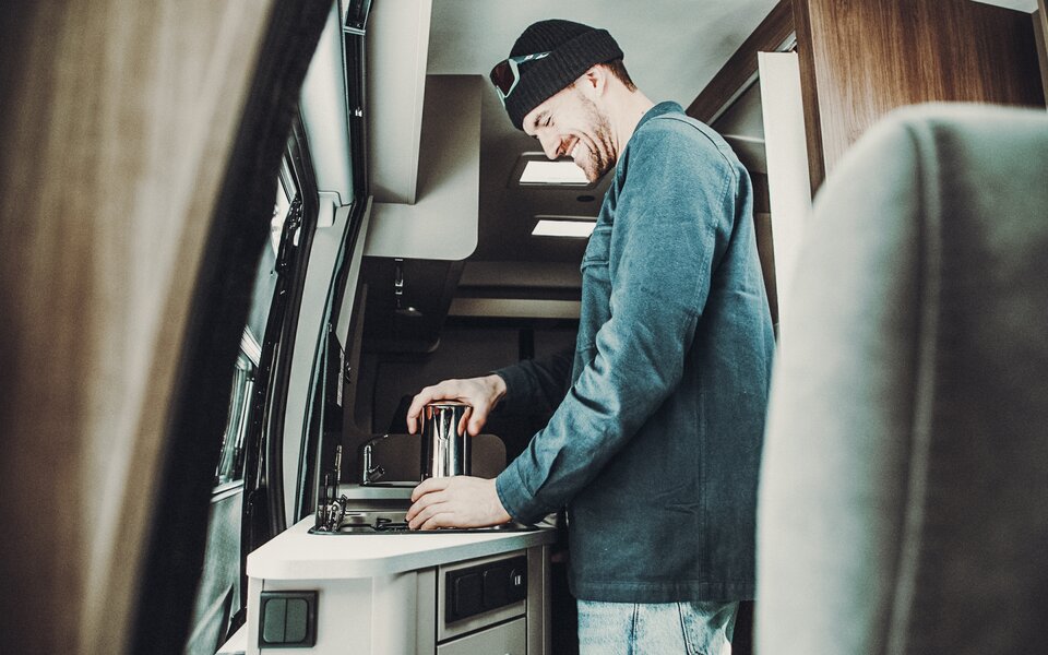 A person in the kitchen of a Carado motorhome with sink and worktop