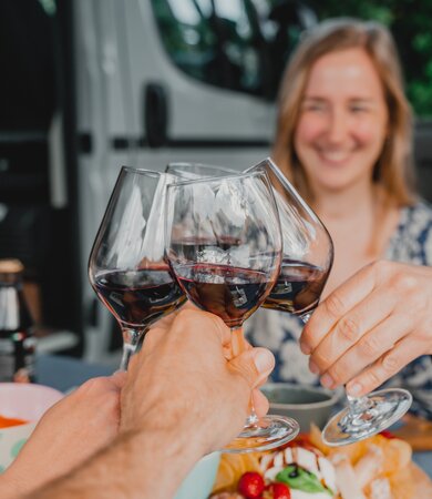 Clinking wine glasses in front of an Etrusco Campervan Fiat Plus, surrounded by snacks and a joyful camping atmosphere in nature.