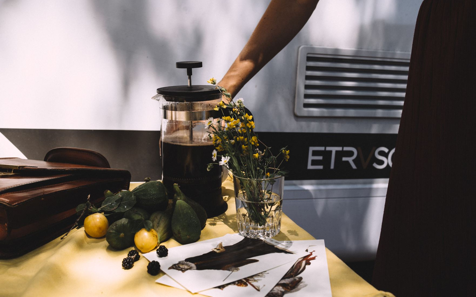 Campingscen med färska citroner, blommor och en kaffekanna på ett bord framför en Etrusco husbil, perfekt för avkopplande stunder.