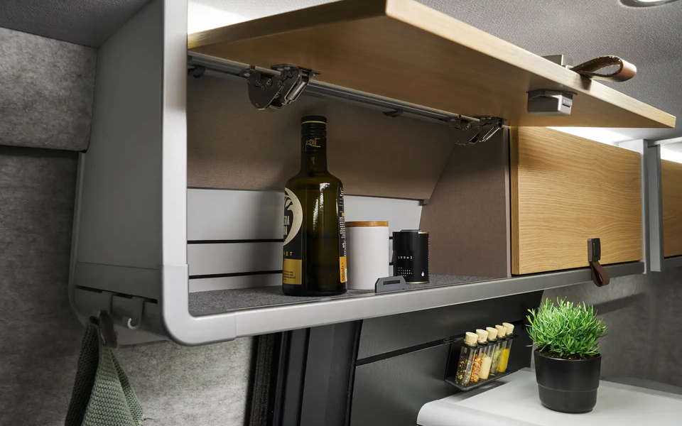 The roof storage cabinet above the kitchen of the HYMER Grand Canyon S in the Pearl Grey style world is open. Oil and spices are visible inside.