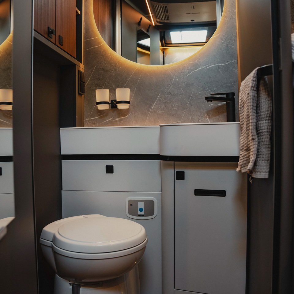 Modern bathroom in the Hymer B‑MC I with illuminated round mirror, premium washbasin, toilet and well‑thought‑out storage concept for comfortable travel