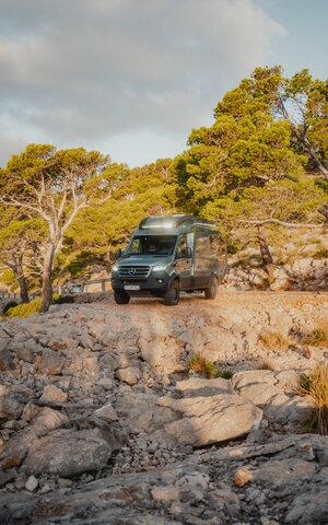 View from the front of the Venture S, headlights on, the vehicle is standing in front of a rocky abyss, surrounded by trees.