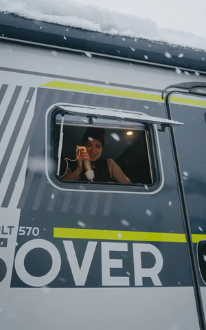 Vy från passagerarsidan utanför in i köksfönstret på HYMER ML-T 570 CrossOver, en kvinna syns i fönstret