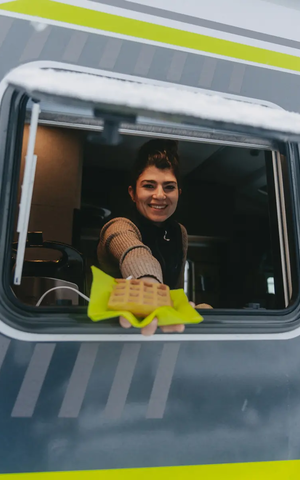 Vy in i köksfönstret på HYMER ML-T 570 CrossOver, en kvinna räcker ut en våffla