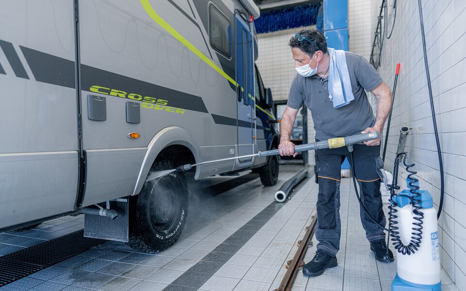 HYMER owner using a jet wash to thoroughly clean the HYMER CrossOver's studded tires in the wash hall.